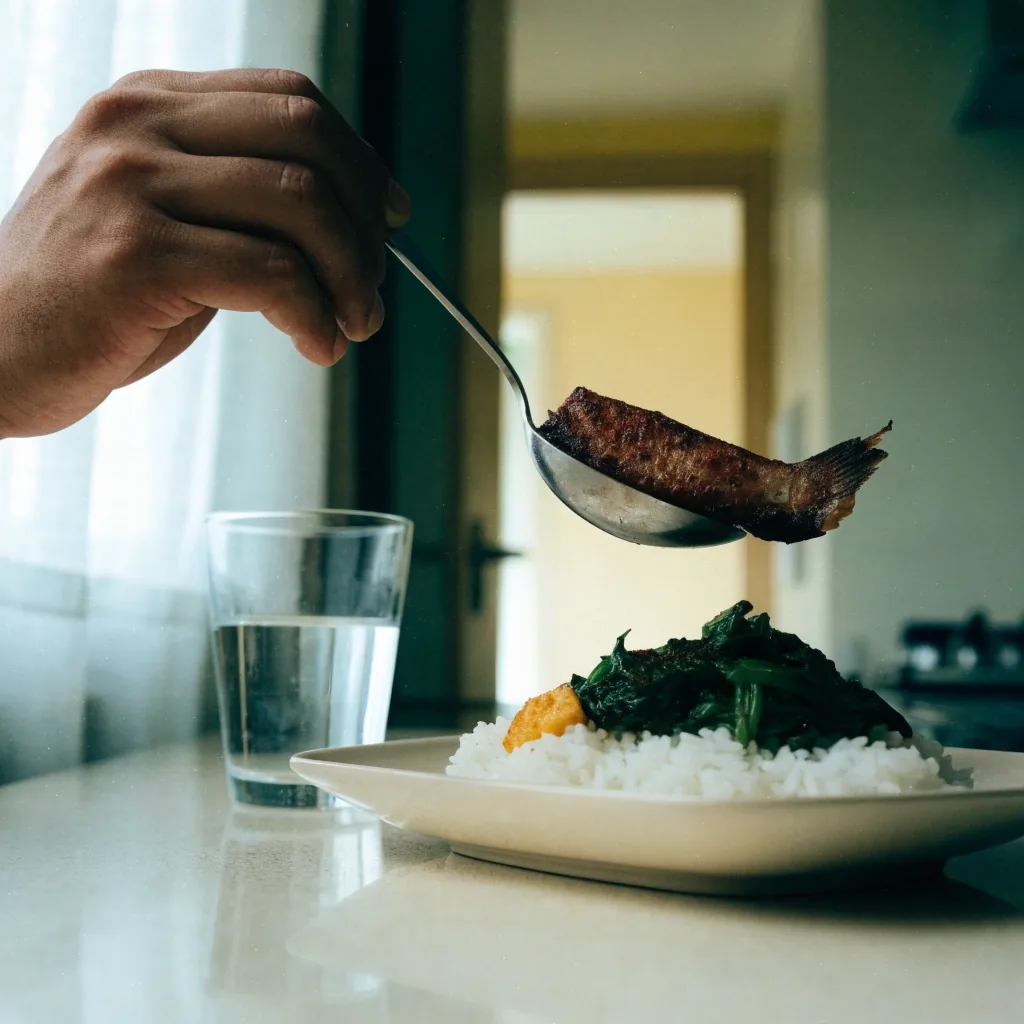 Hands lifting a portion of grilled fish from a plate of rice and greens